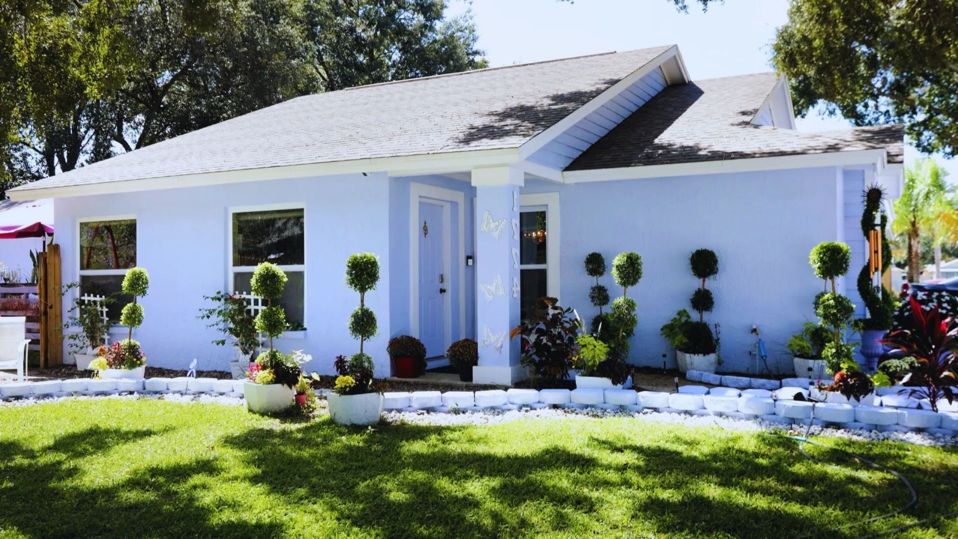  A blue house with white trim surrounded by green bushes in a sunny outdoor setting.
