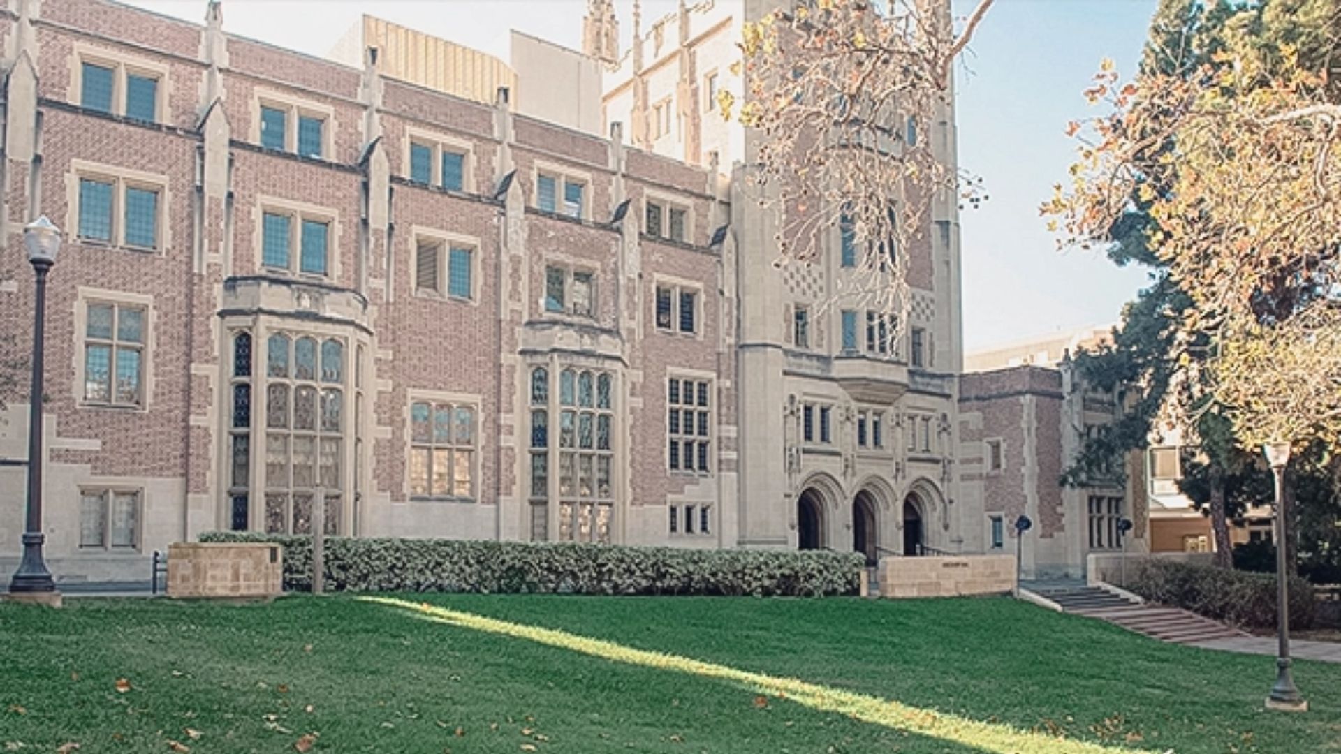 A large brick building stands behind a well-maintained lawn, showcasing its architectural features and green surroundings.