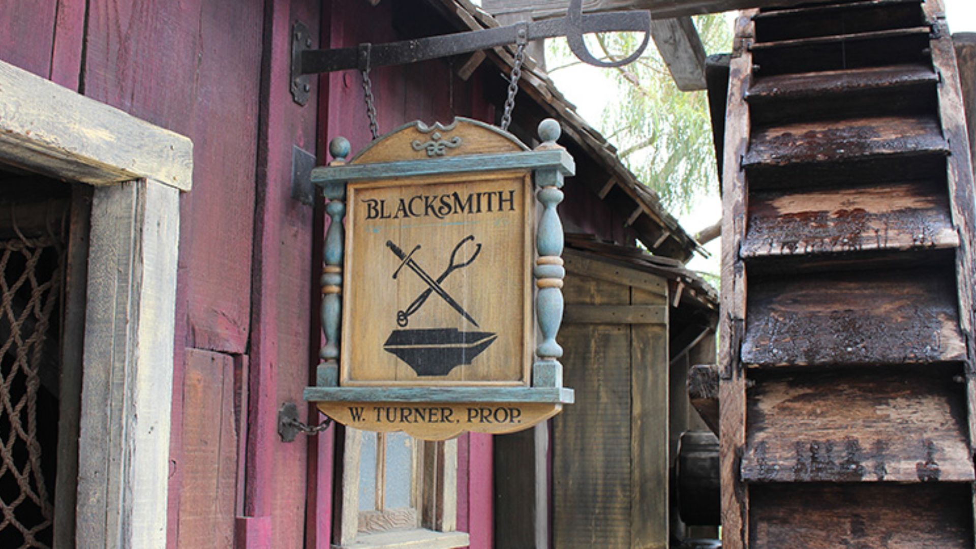 A sign hangs from a building, with a ladder leaning against the side for access.