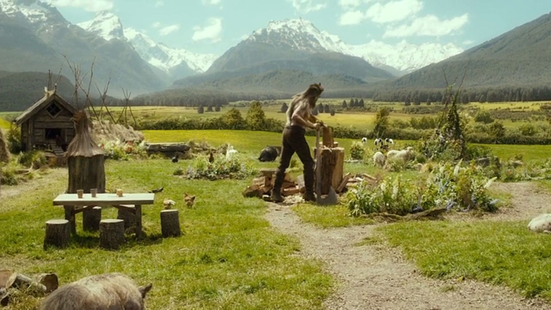 A man stands in front of a hut surrounded by various animals, showcasing a rural or farm setting.
