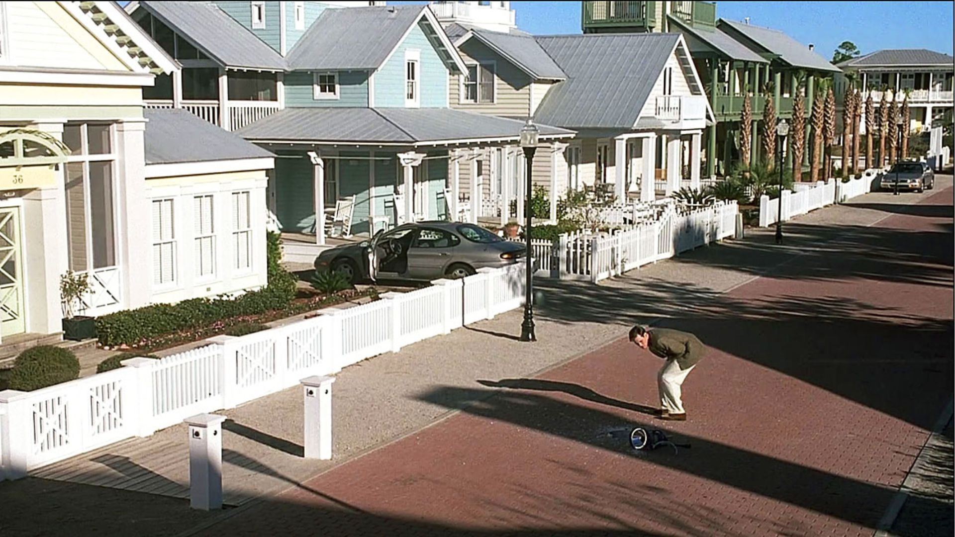 A man skateboards down a street lined with houses, showcasing his skills in a suburban neighborhood.