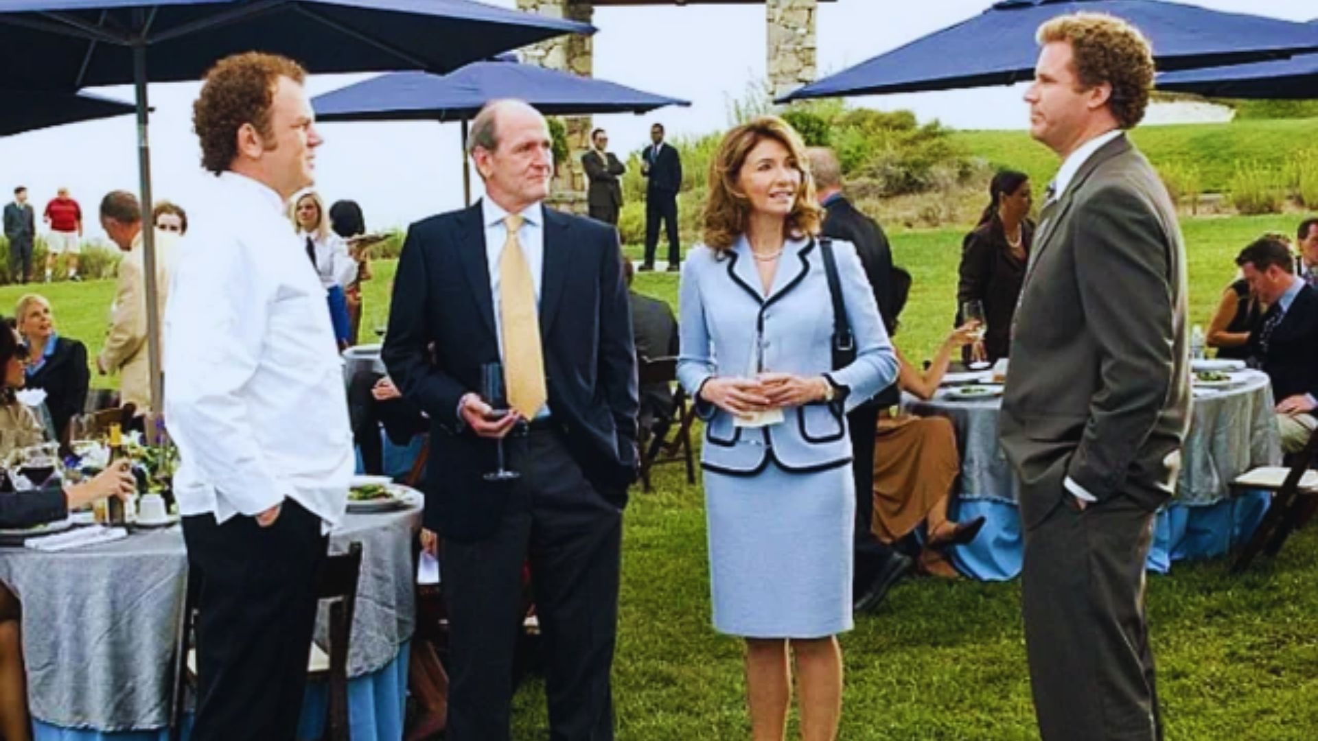  A group of people gathered around a table, each holding umbrellas, engaged in conversation outdoors.
