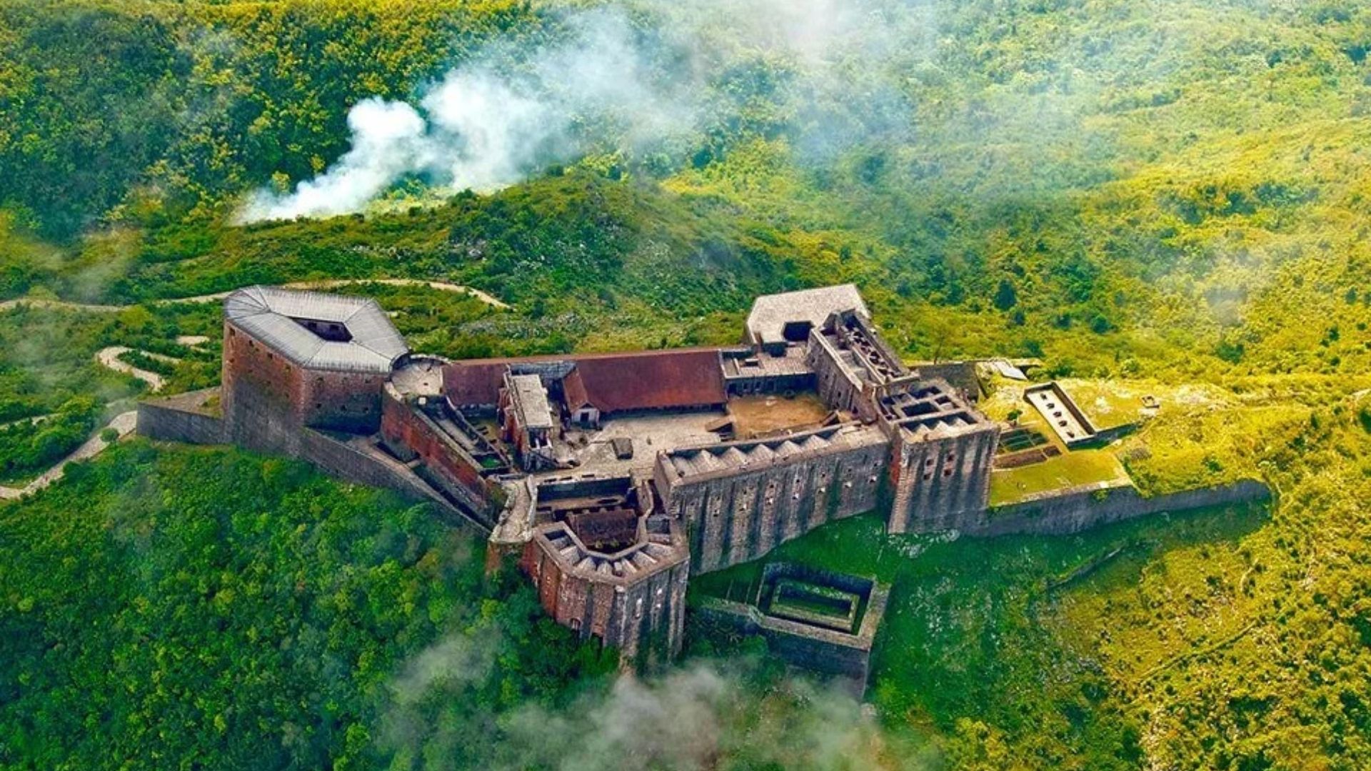 Aerial view of a castle surrounded by lush green forest, showcasing its majestic architecture amidst nature.