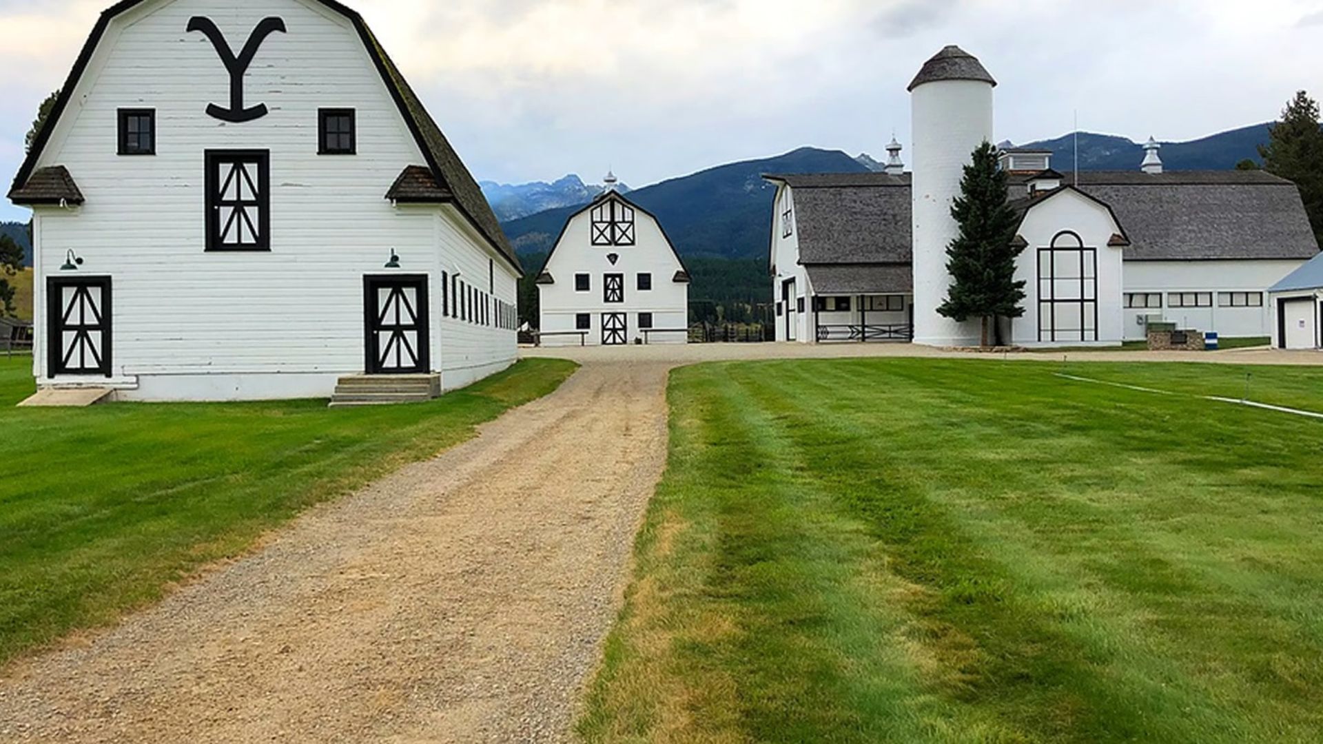 A scenic farm featuring two white barns alongside a dirt road surrounded by open fields.