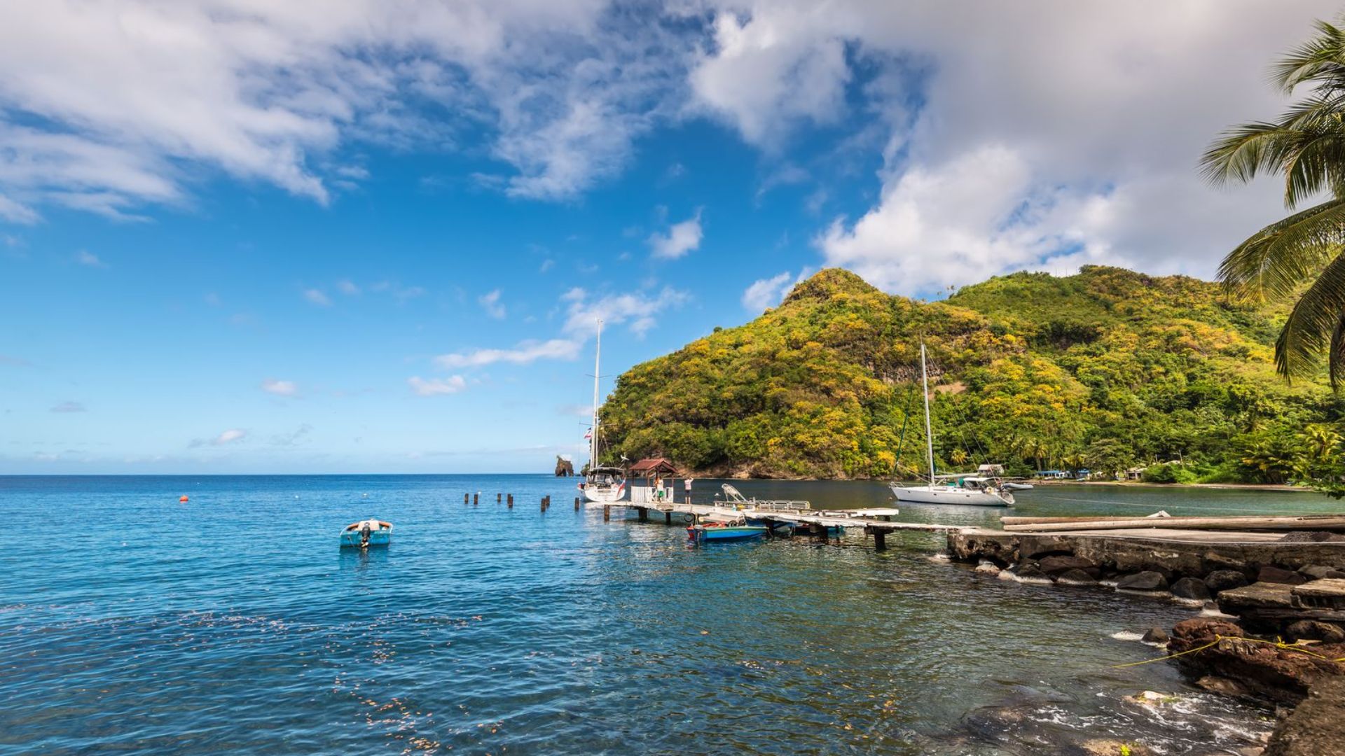 A scenic view of a tropical island featuring palm trees and boats on clear blue waters under a bright sky.