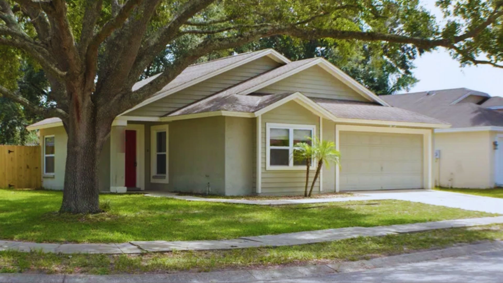 A house with a garage and a tree in the front yard, showcasing a welcoming suburban landscape.

