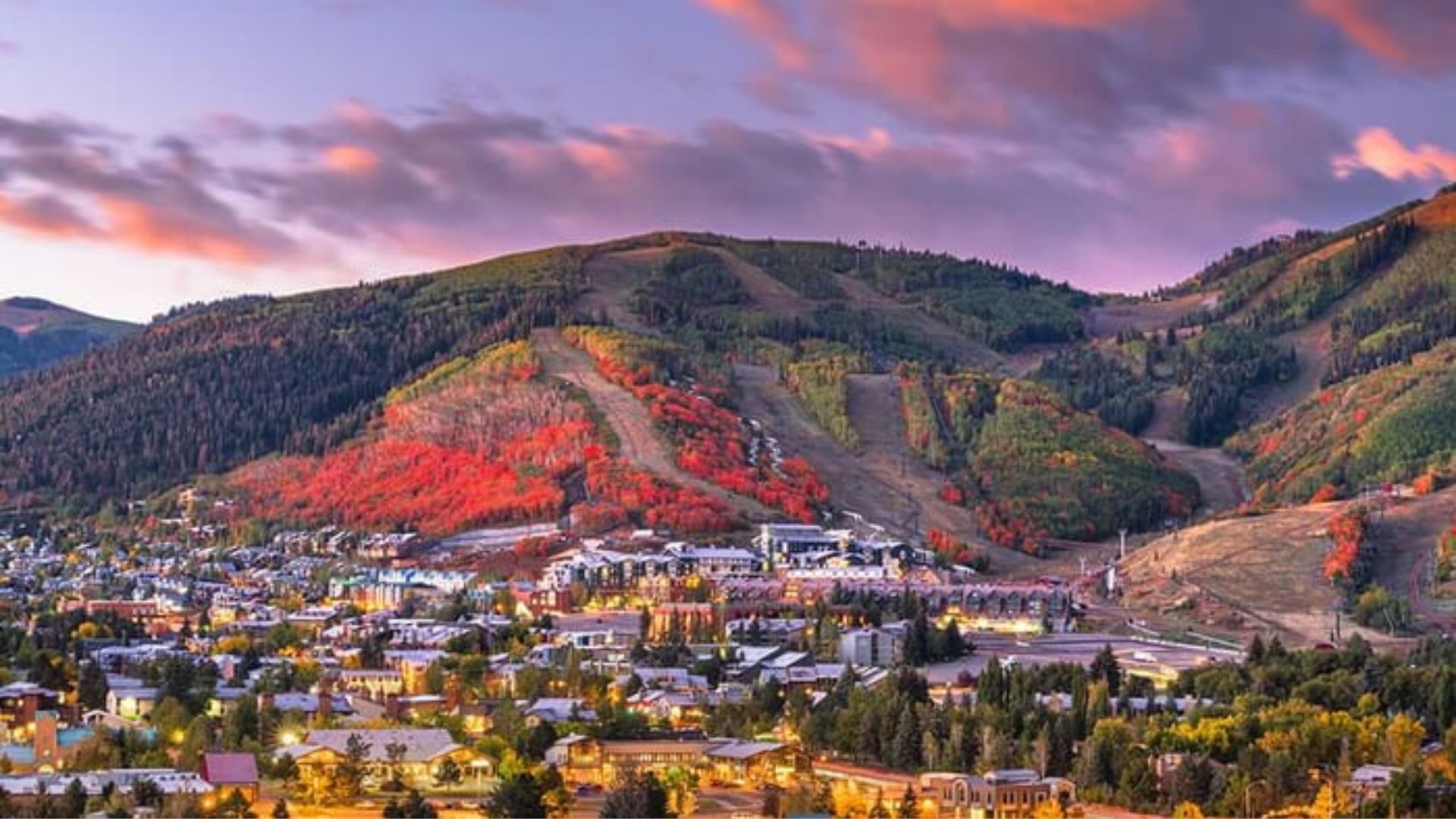Scenic view of a mountain town, showcasing charming buildings nestled among lush green hills and towering peaks.
