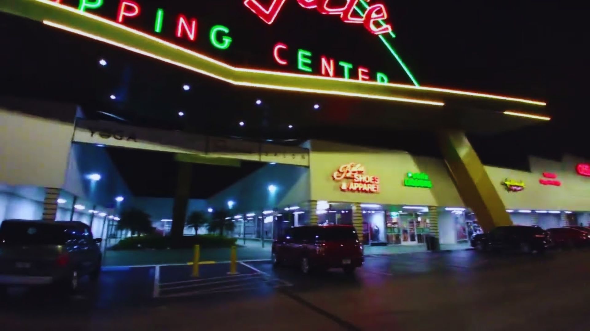 The brightly lit entrance of a shopping center at night, showcasing illuminated signs and welcoming atmosphere.
