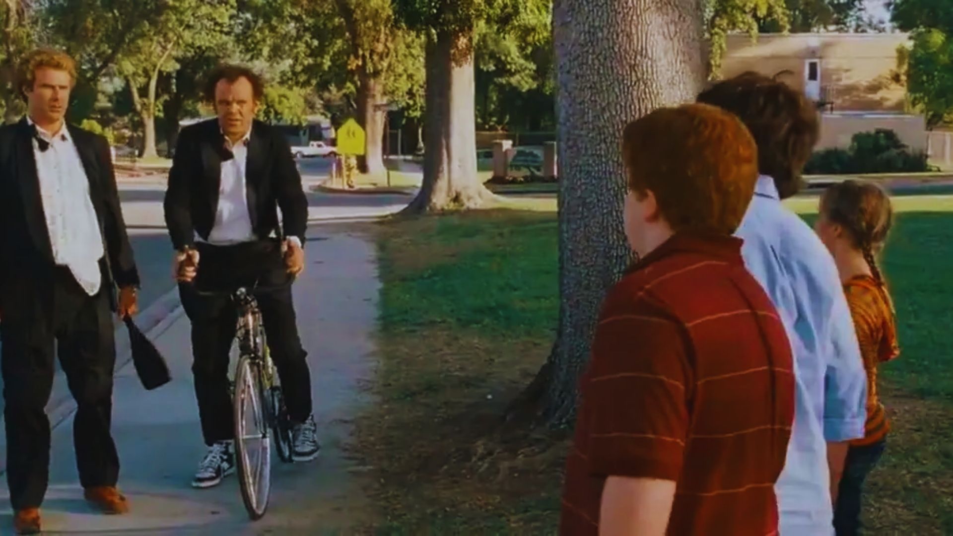 A group of people gathers around a man on a bike, engaging in conversation and enjoying the outdoor setting.
