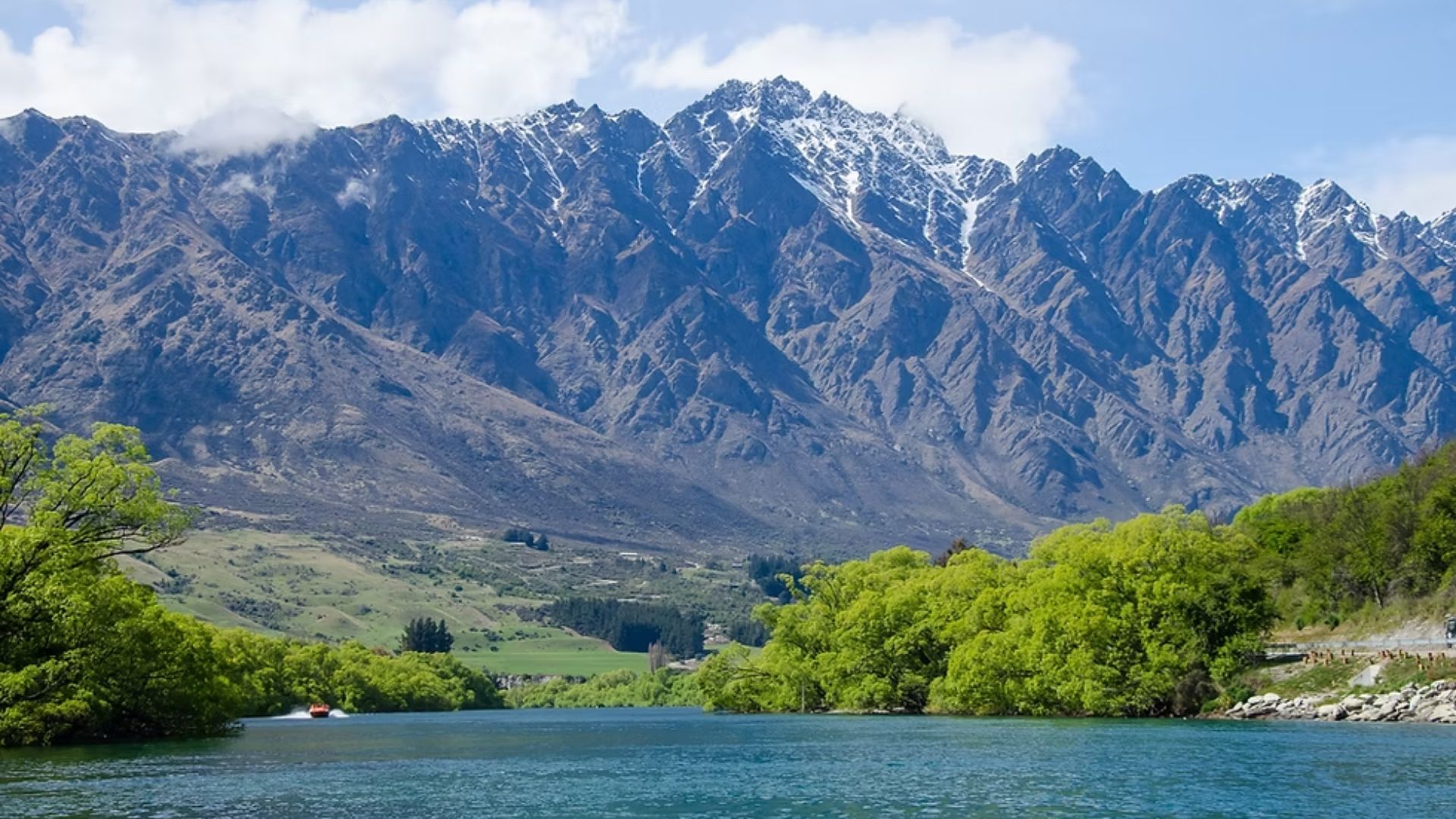 A serene river flows through a landscape with mountains in the background and lush trees lining the banks.