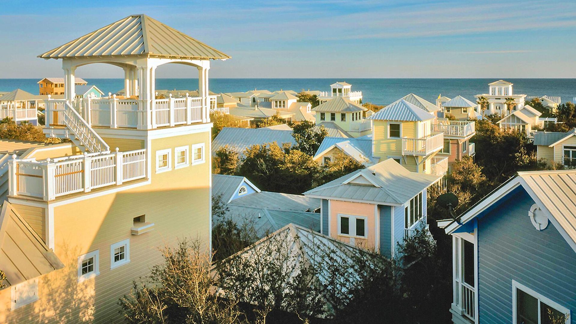 A sunny beach view featuring sand, waves, and colorful houses lining the shore.