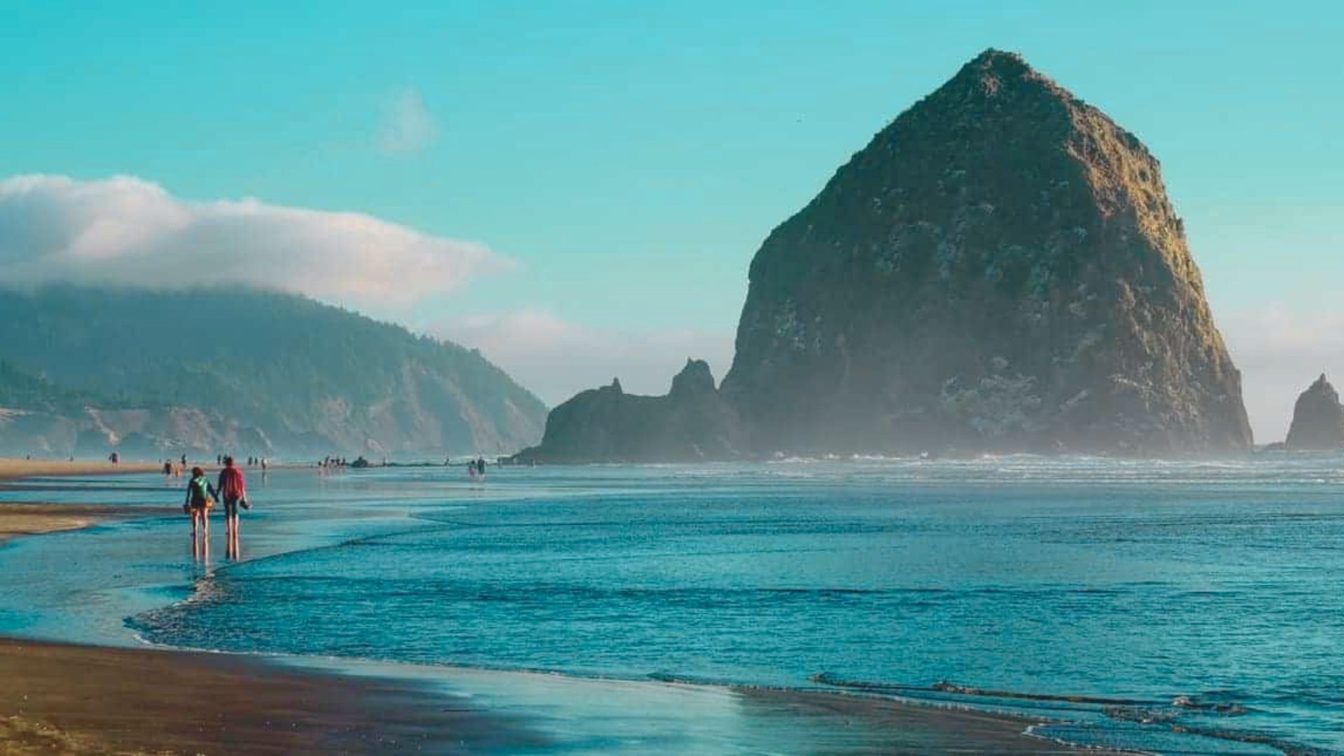  Haystack Rock rises majestically at Cannon Beach, Oregon, surrounded by sandy shores and gentle ocean waves.