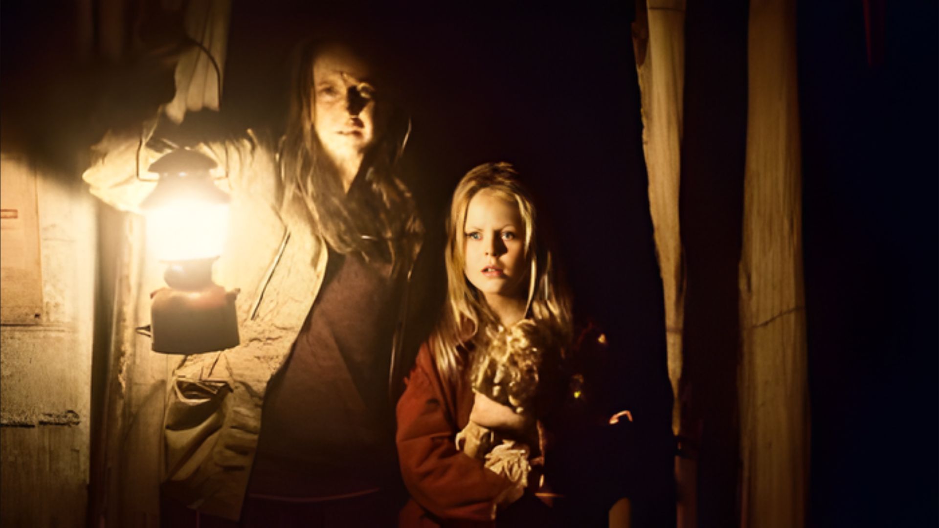 Two women stand together in a dark setting, illuminated by a soft light behind them.