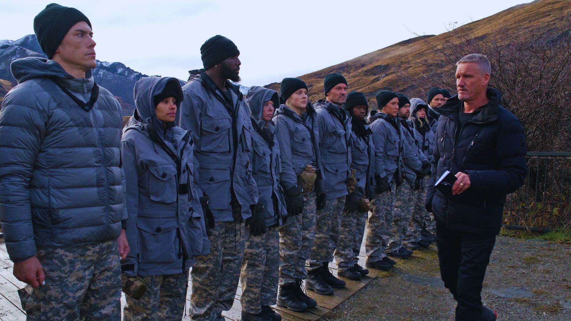 A group of soldiers stands in formation in front of a majestic mountain backdrop.