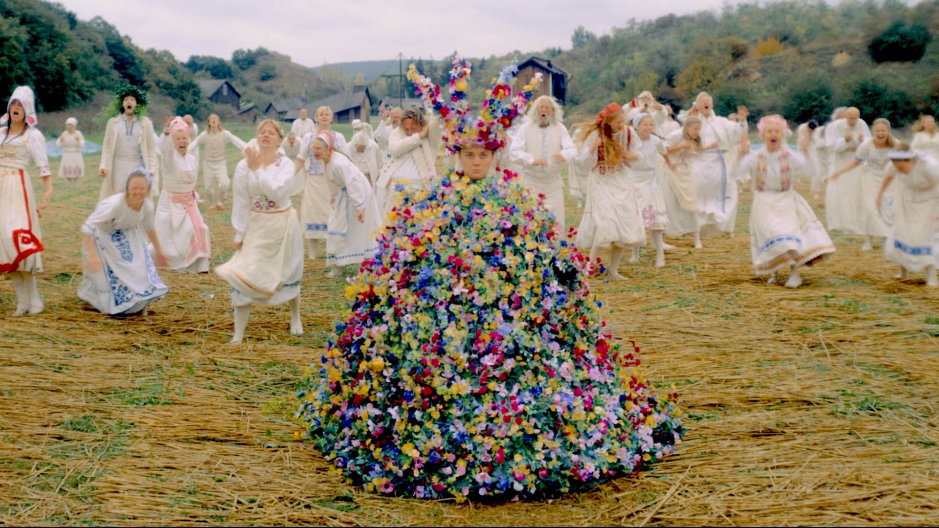 A group of people wearing white dresses adorned with flowers in their hair, standing together in a cheerful setting.