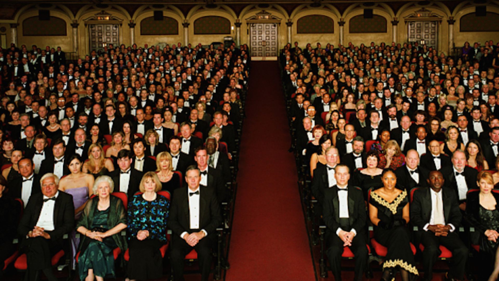 A large group of people in tuxedos seated in a spacious auditorium, engaged in conversation and enjoying the event.
