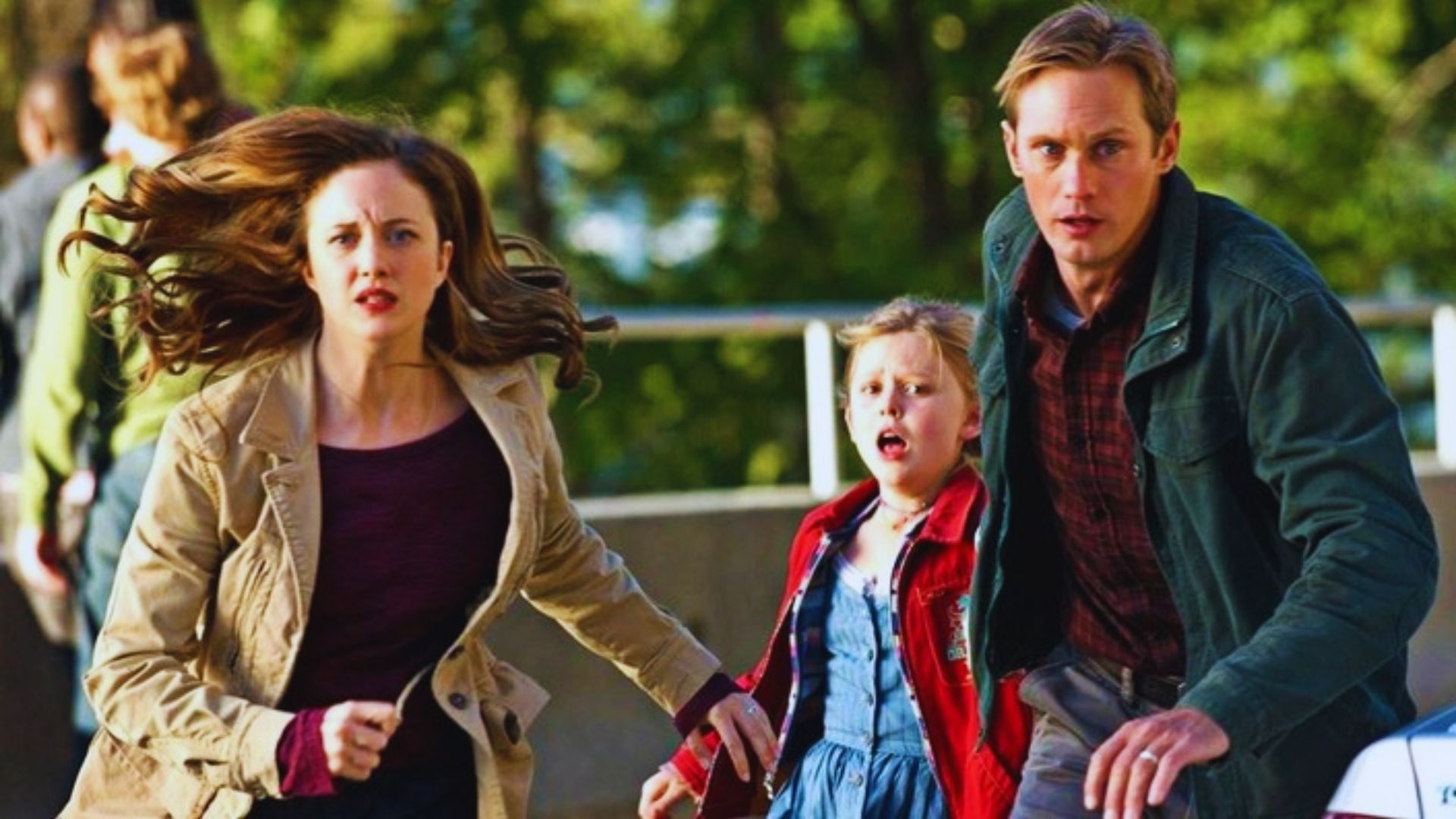 A man and woman run alongside two children in a park, enjoying a sunny day together.