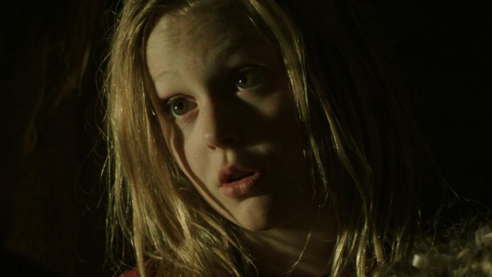 A young girl with long blonde hair gazes intently at an unseen object, her expression curious and engaged.