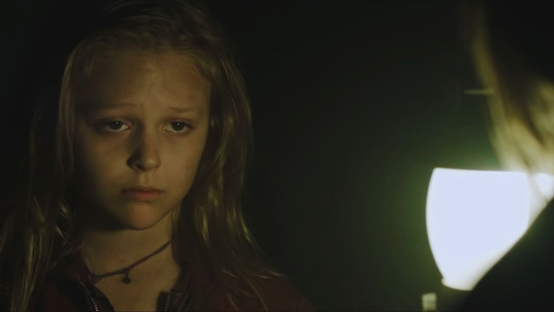 A young girl gazes at the camera, her face illuminated against a dark background.