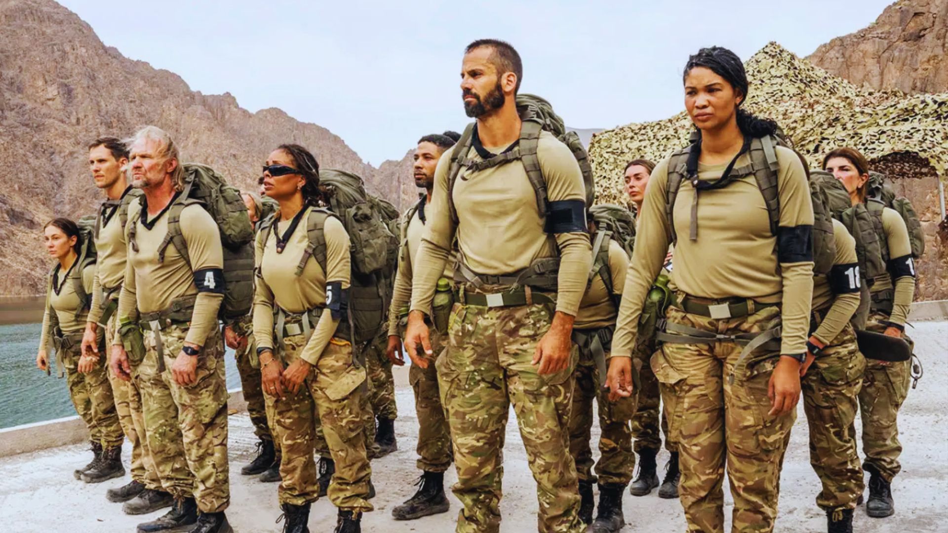 A group of soldiers stands in formation in front of a majestic mountain backdrop.