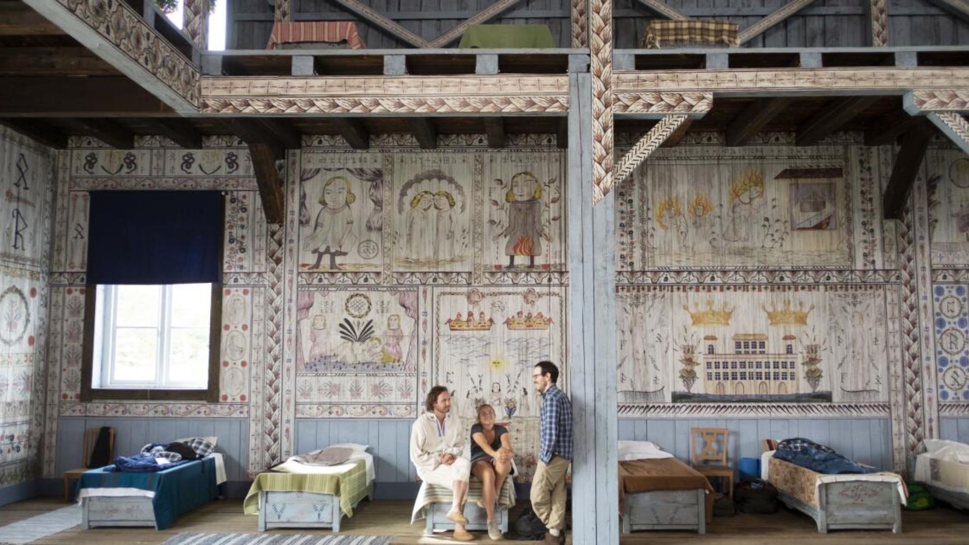 A family stands together in a room featuring a bed and a wall adorned with various paintings.
