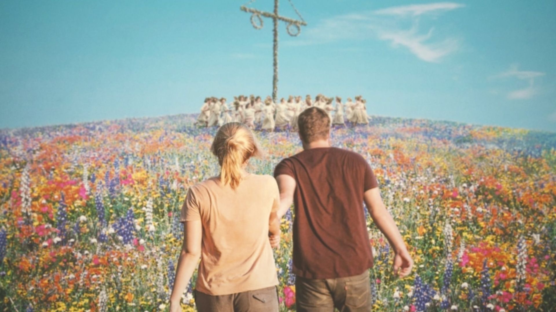  A man and woman stroll through a vibrant field filled with colorful flowers under a clear blue sky.