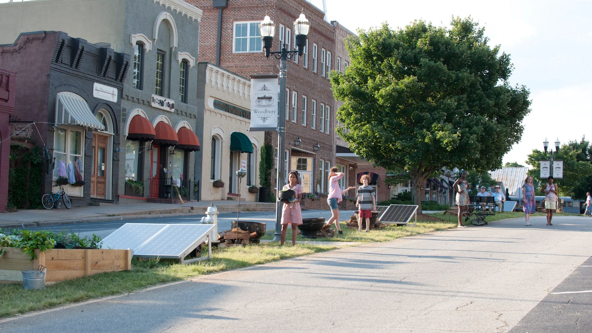 A bustling street scene in Woodbury, featuring shops and pedestrians walking along the sidewalk, a key filming location for The Walking Dead.
