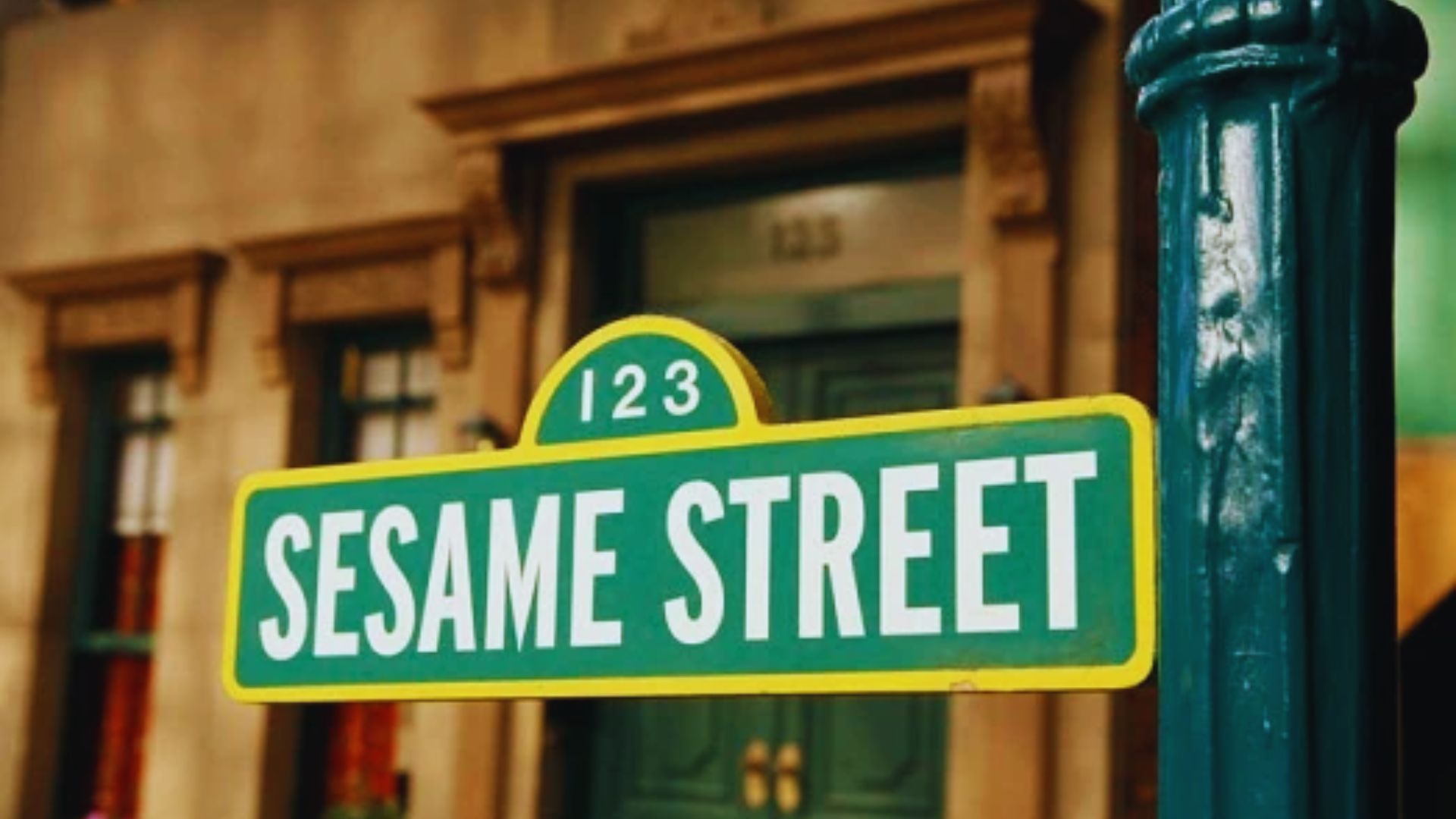 Sesame Street signboard mounted beside a green pillar in a classic urban street setting.
