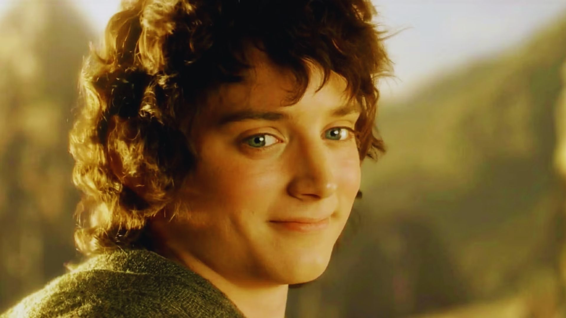 A young person with curly brown hair and blue eyes smiles softly against a blurred mountainous background, conveying a sense of calm and serenity.