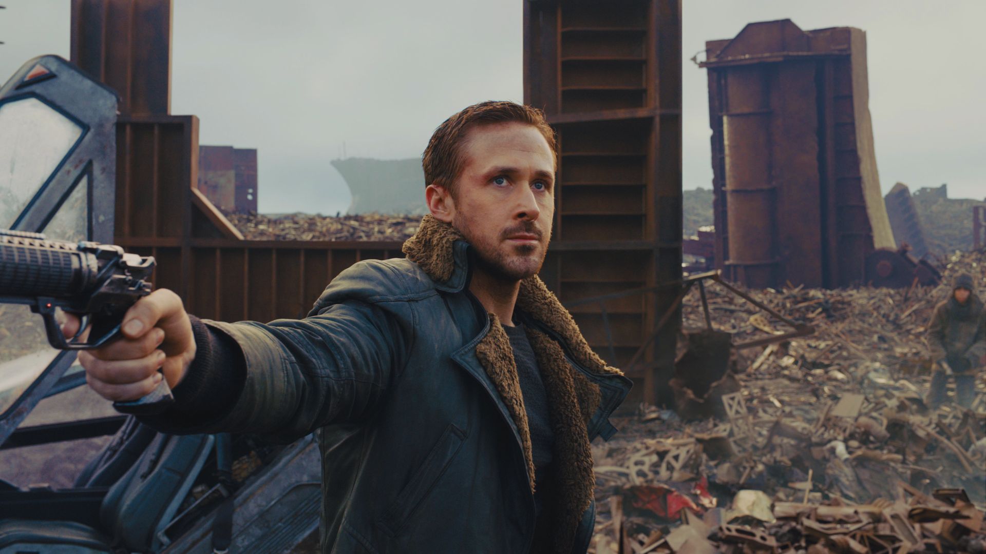 A man in a futuristic coat stands in a junkyard, aiming a gun with determination. The scene has a gritty, dystopian feel with scattered debris.