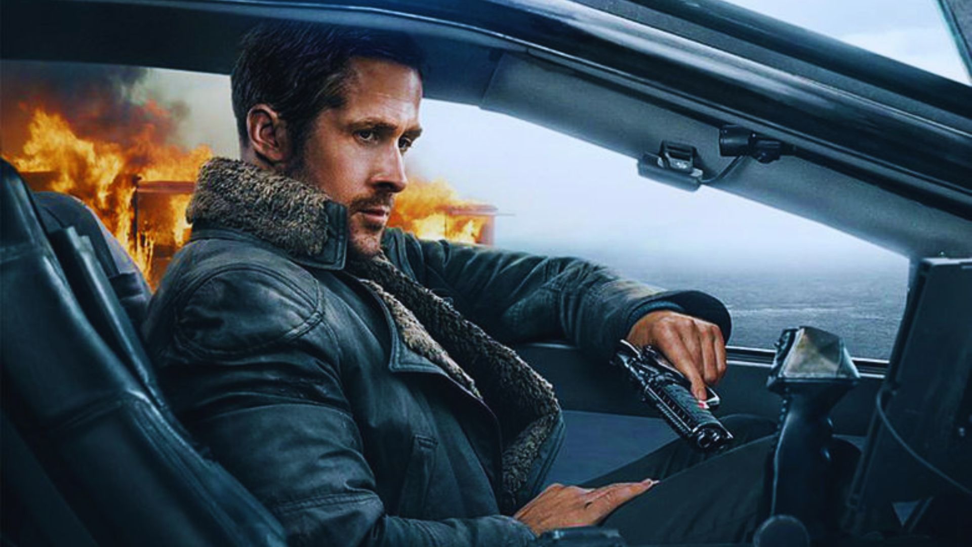A man with a serious expression sits in a futuristic car, holding a gun. A building burns in the background, creating a tense, dramatic scene.