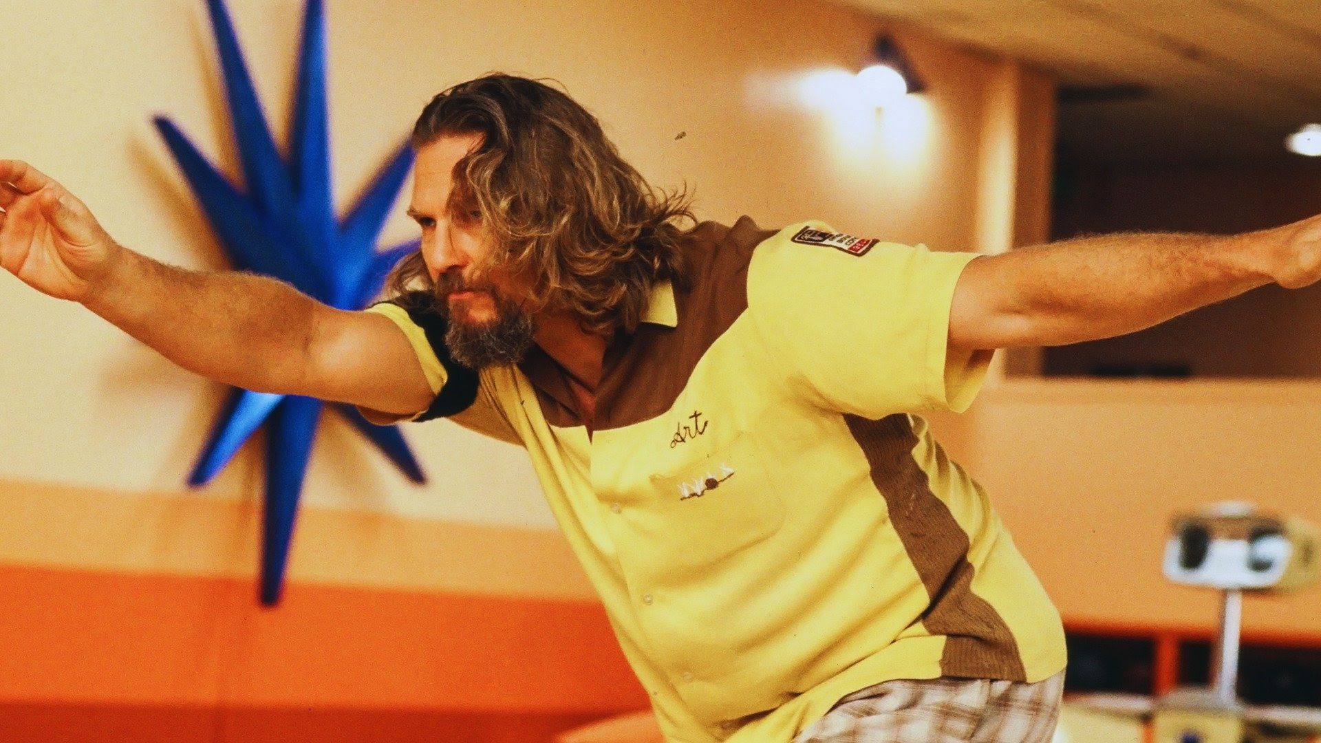 A man with long hair and a beard is bowling, wearing a yellow and brown shirt. His expression is focused, arms extended, highlighting his concentration.