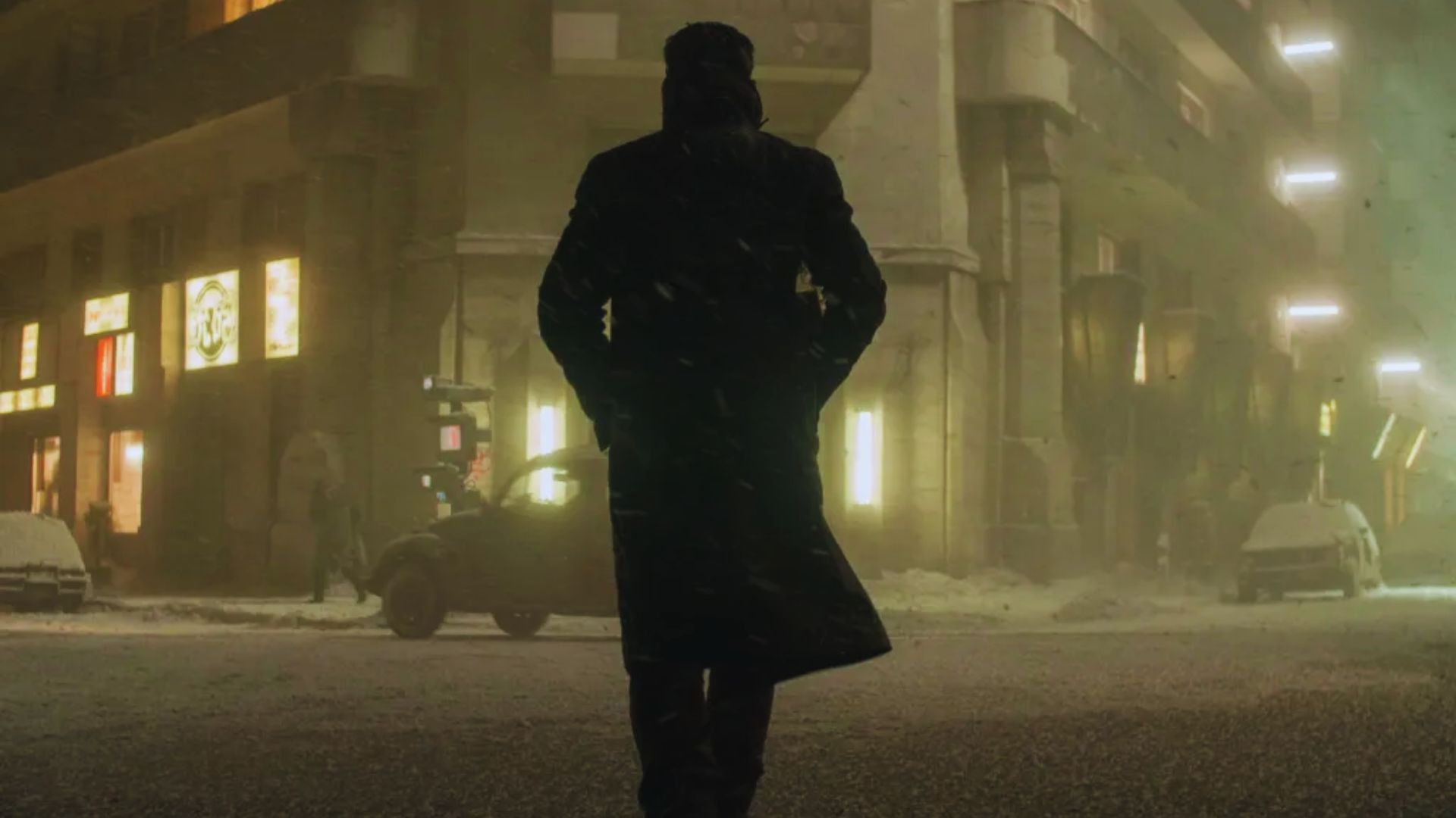 A person in a long coat walks down a snowy, dimly lit urban street at night, evoking a mysterious and solitary atmosphere. Retro cars and neon lights line the street.