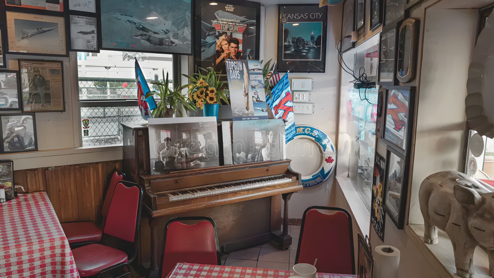 Cozy diner corner with a vintage wooden piano adorned with framed photos and flags. Red checkered tablecloths, red chairs, and nostalgic wall art create a warm, nostalgic vibe.