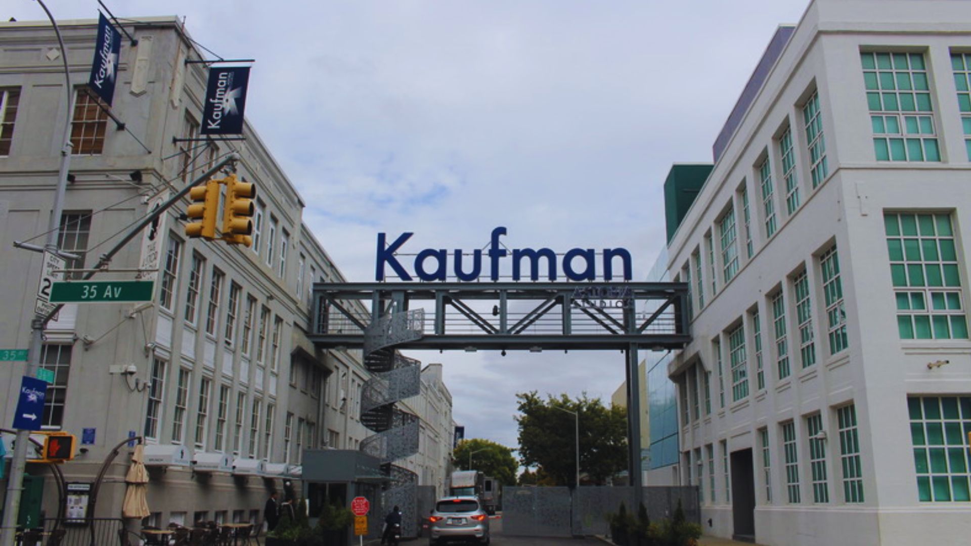 Kaufman Astoria Studios entrance with overhead sign, city street, and surrounding buildings in an urban setting.