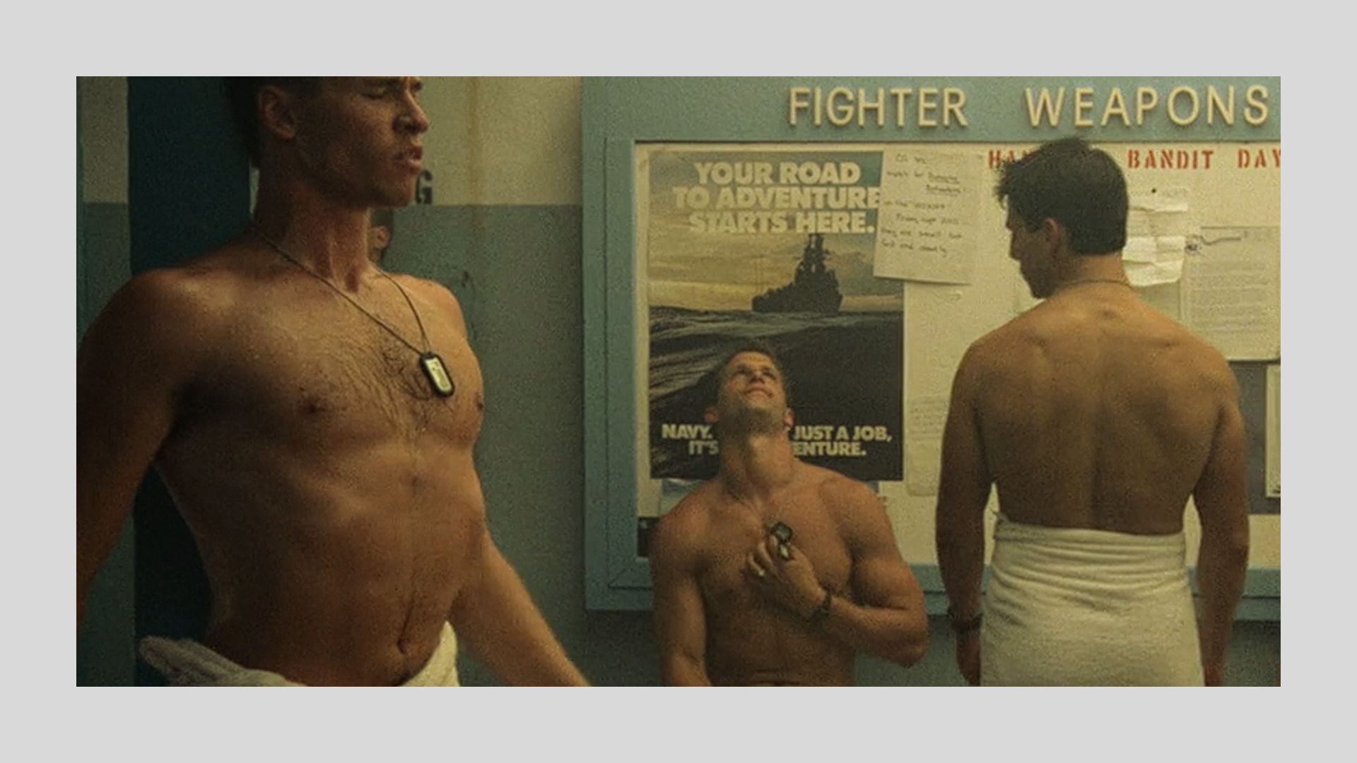 Shirtless men in a locker room, wearing towels, with military-themed posters on the wall. The scene conveys a serious and competitive tone.