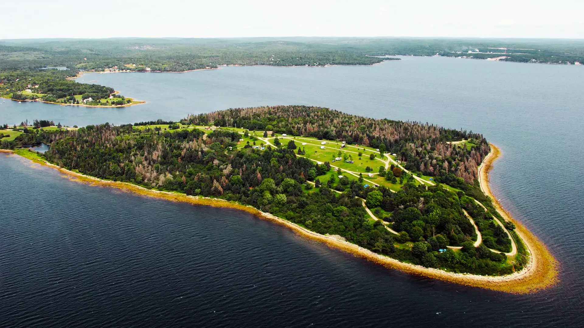 Oak Island aerial with campgrounds, winding paths, dense forest, and rocky Mahone Bay coast.