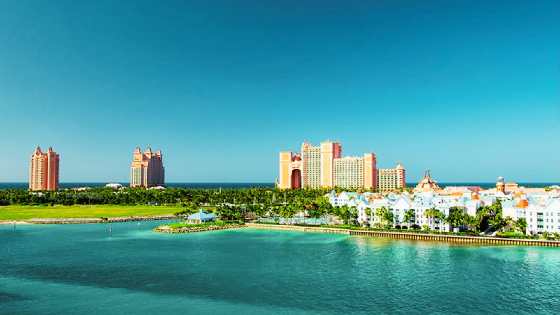 Pink resort towers with archway sit behind white buildings along turquoise waterfront under clear sky