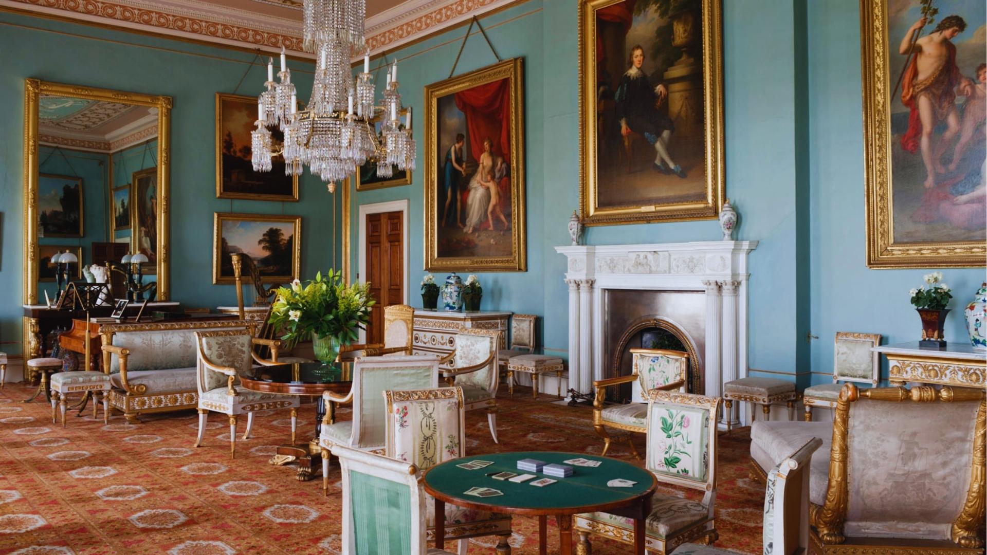 Bridgerton drawing room with powder-blue walls, crystal chandelier, gold-framed portraits, and Regency-era gilded chairs.