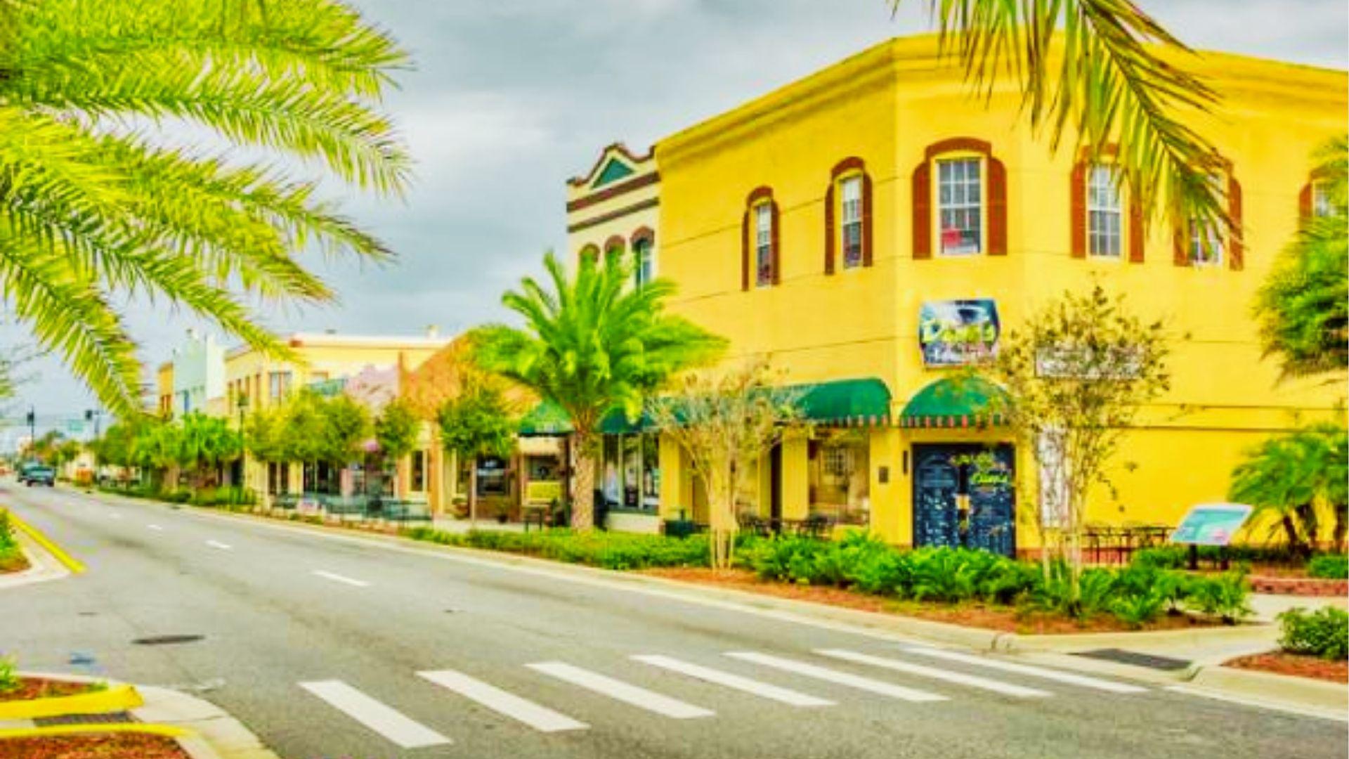 Yellow historic buildings with green awnings line street with palm trees and white crosswalk markings