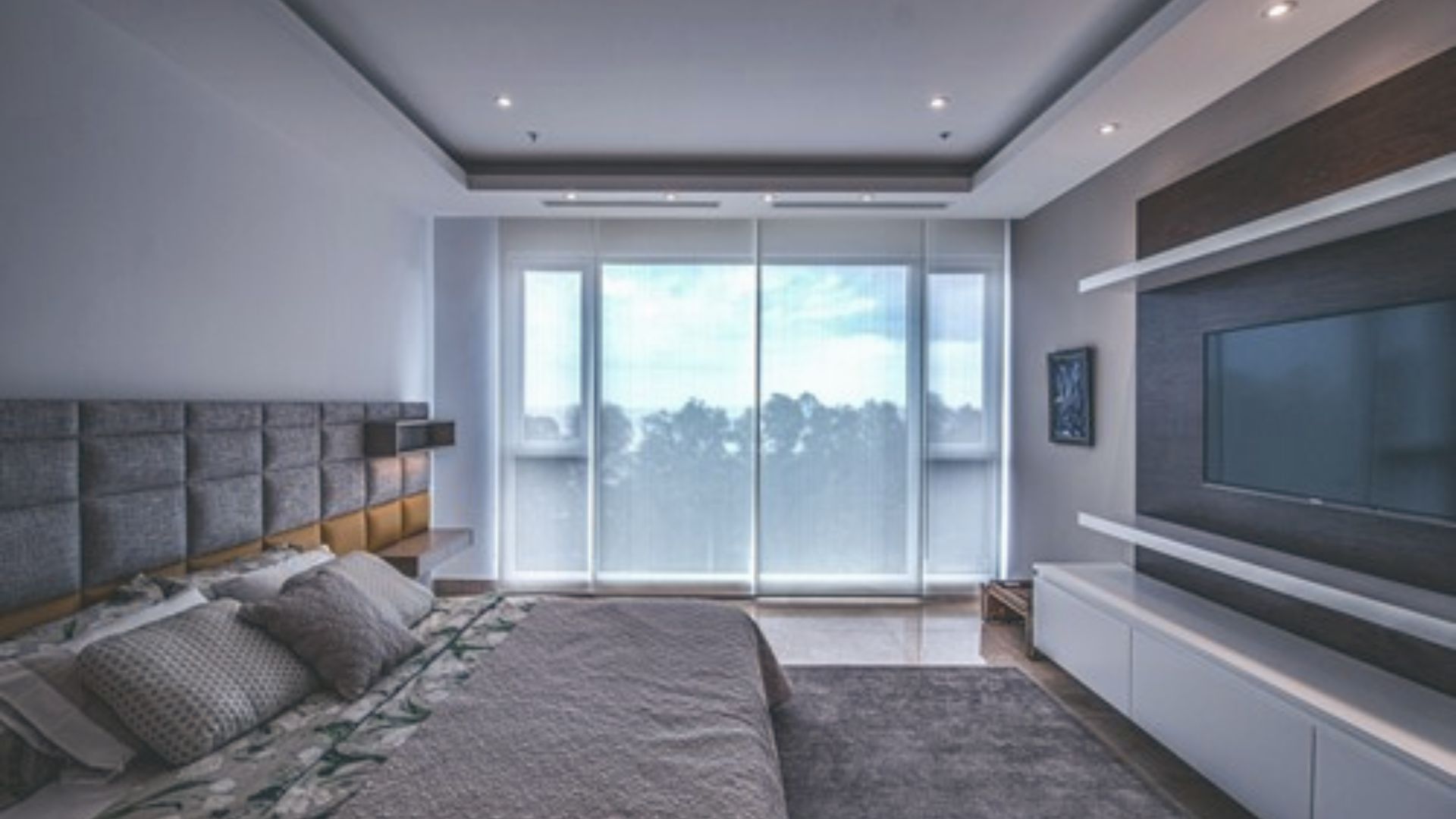 Bedroom with a wall-mounted TV for in-bed viewing across from a padded headboard.