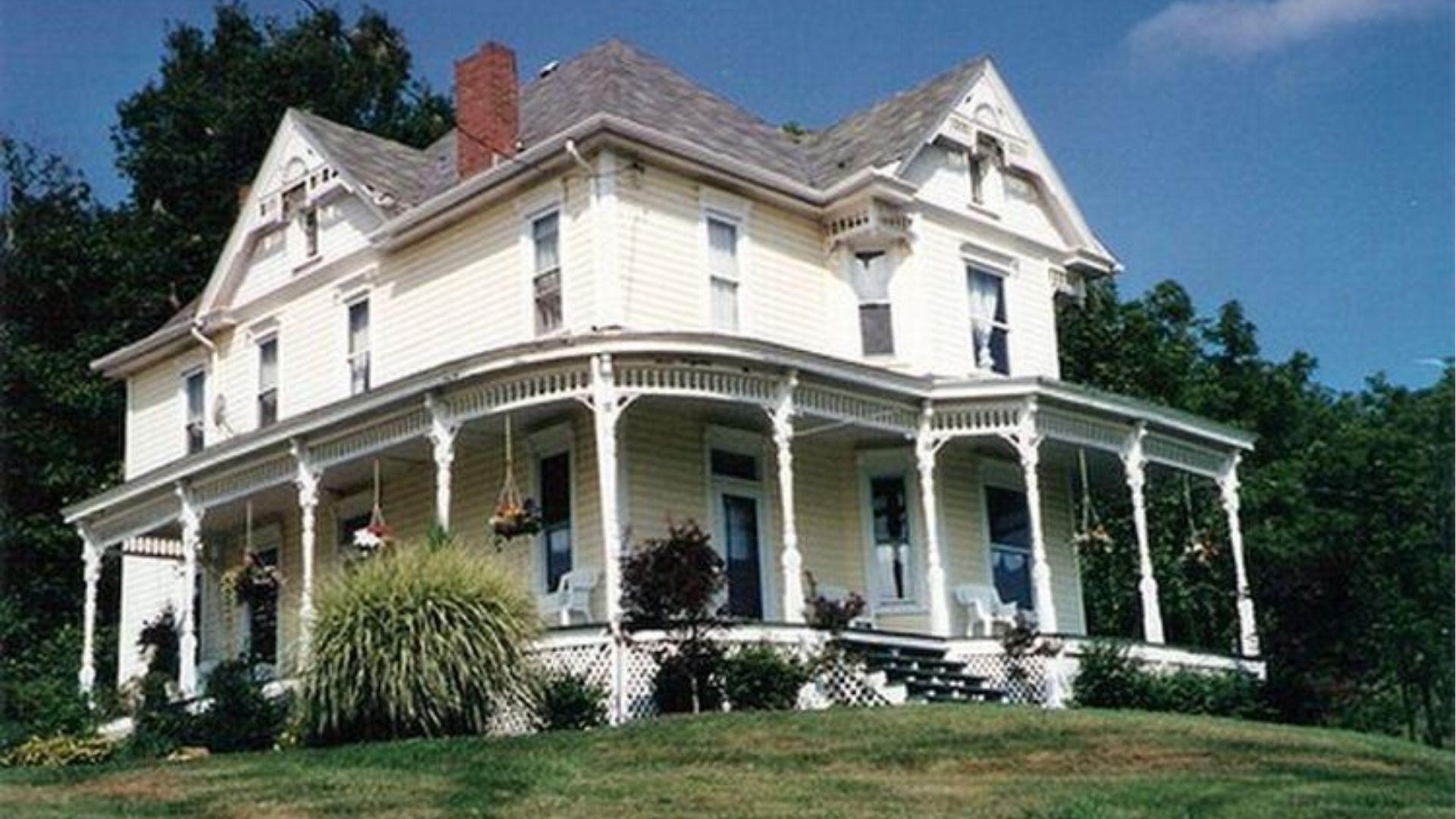 Yellow Victorian farmhouse with wraparound porch in Evans City, PA, the famous house location from the 1968 film.