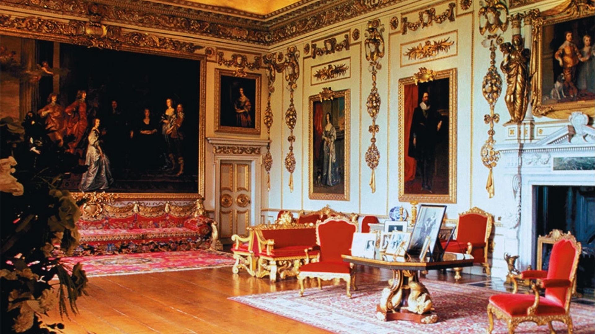 Opulent Bridgerton sitting room with gilded moldings, red velvet sofas, and large oil paintings in gold frames.