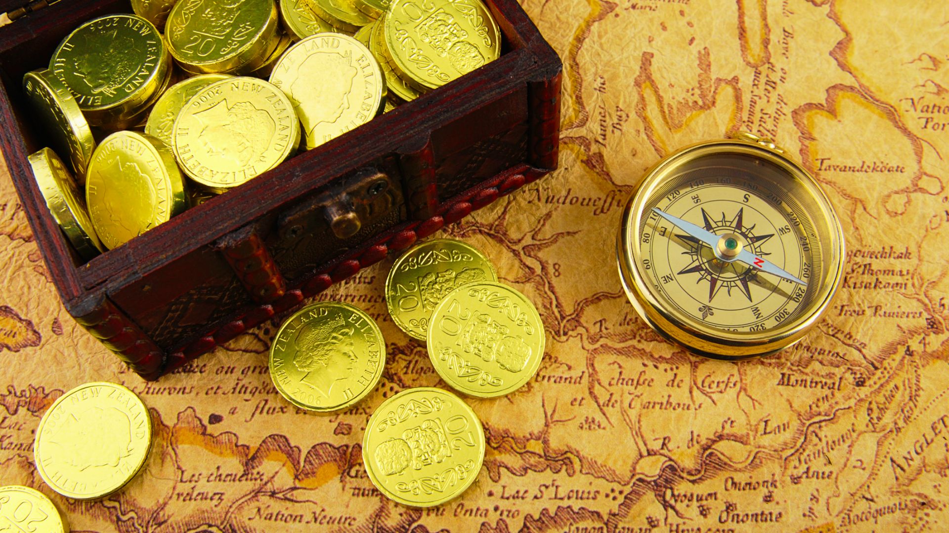 Gold coins spilling from chest beside compass on old map, symbolizing Oak Island treasure.