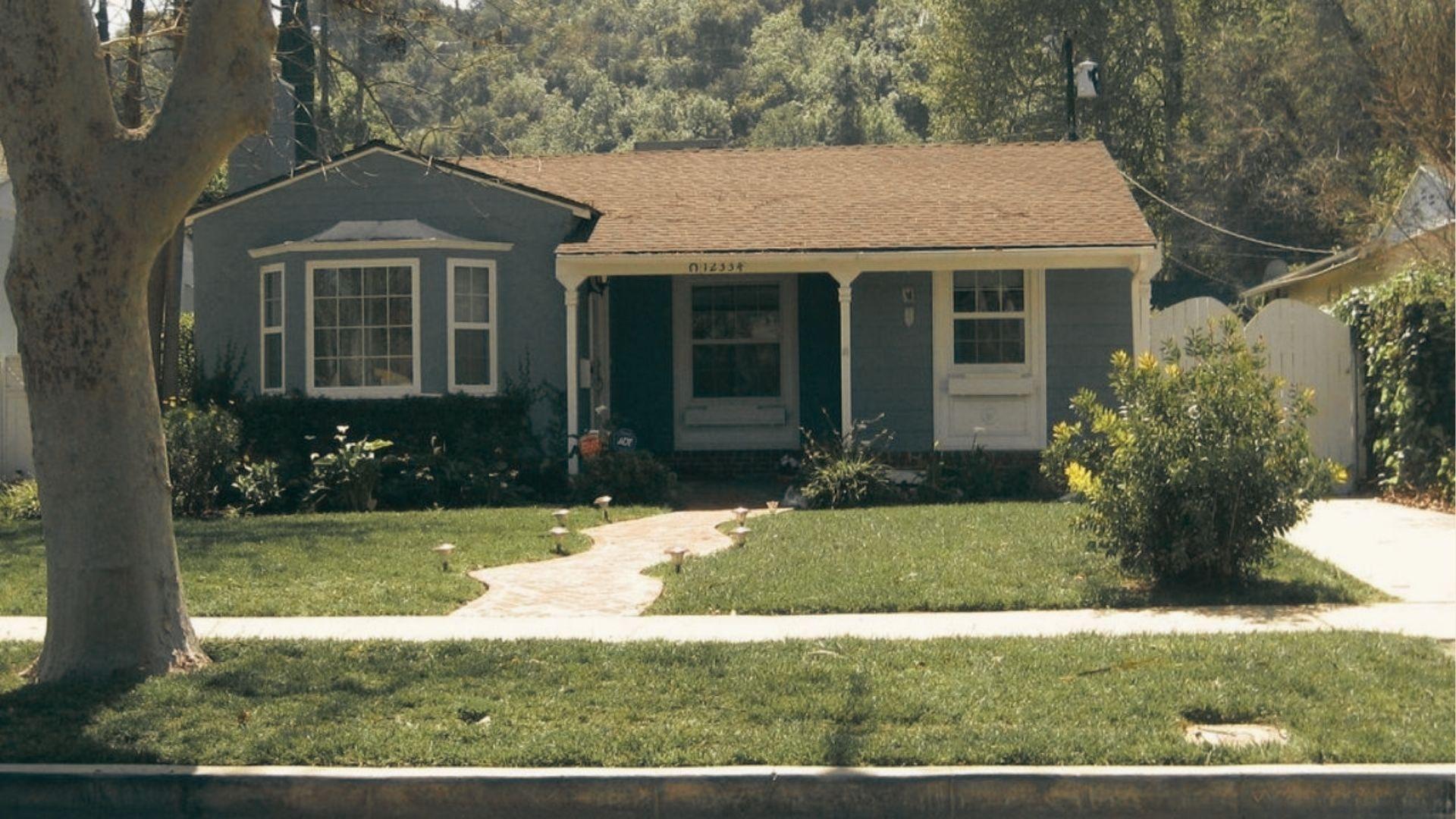 A single-story blue house with a bay window and curved walkway, typical of the Midwest-style homes on Blondie Street.