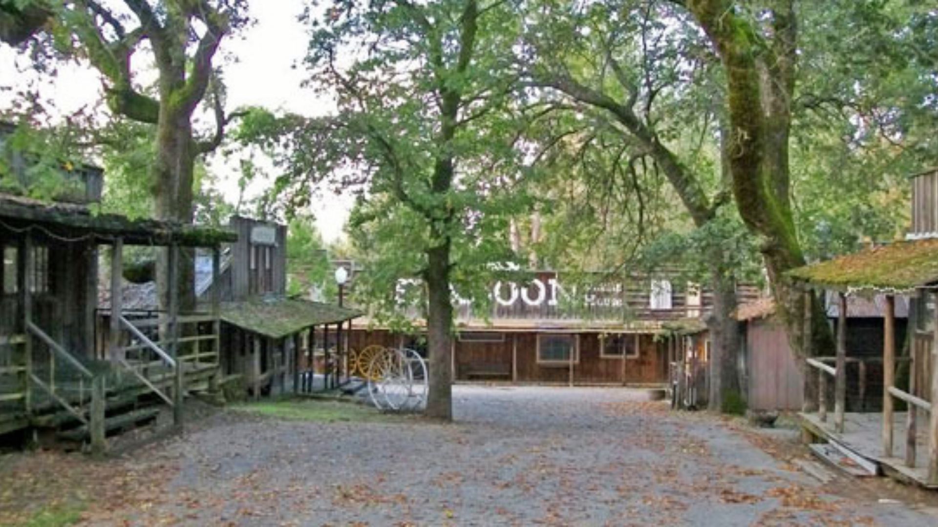 Old West town set shaded by large oaks, with a saloon and wooden boardwalks.