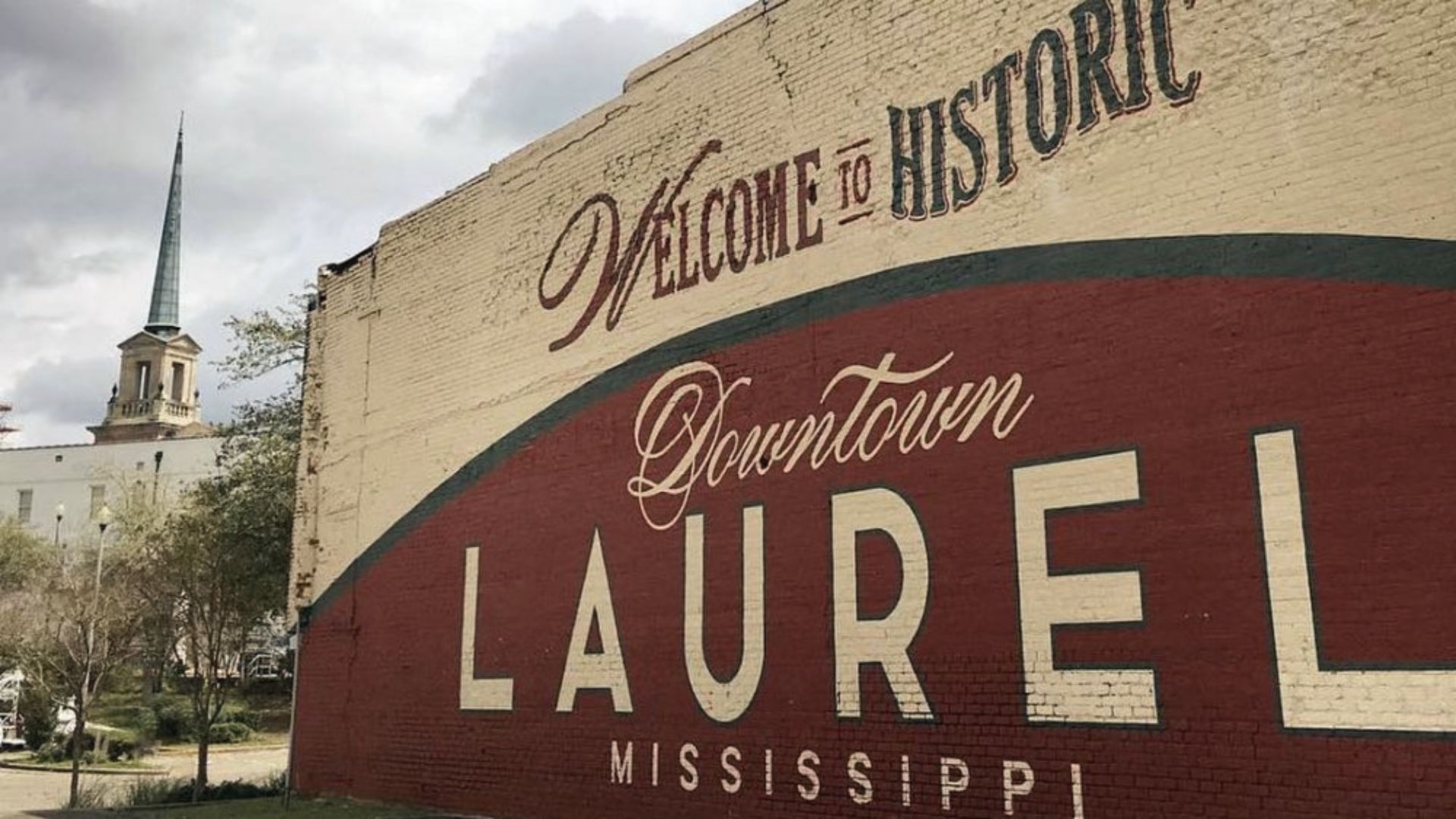 Large painted brick mural reading "Welcome to Historic Downtown LAUREL MISSISSIPPI" with a church steeple behind.