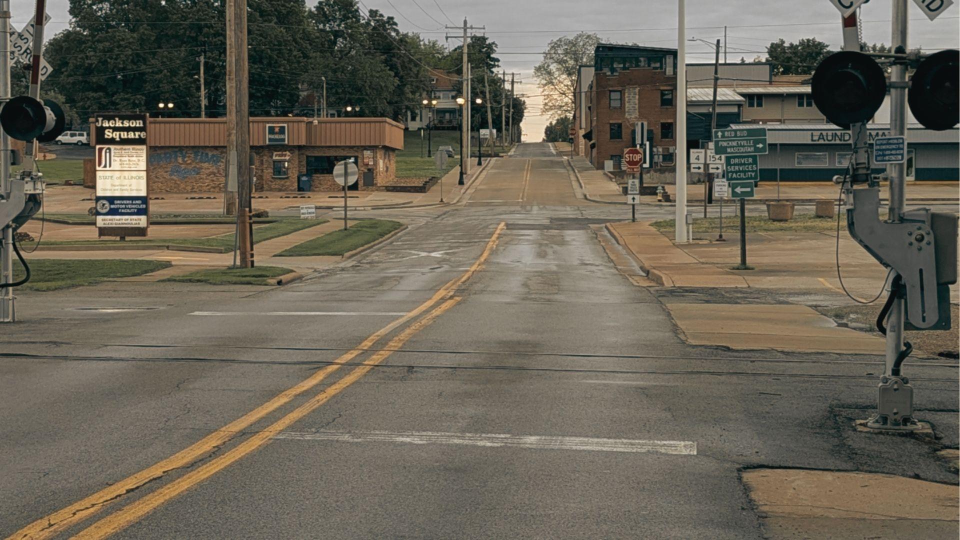 A wet street crosses railroad tracks at Jackson Square, with laundromat and storefronts in the distance.