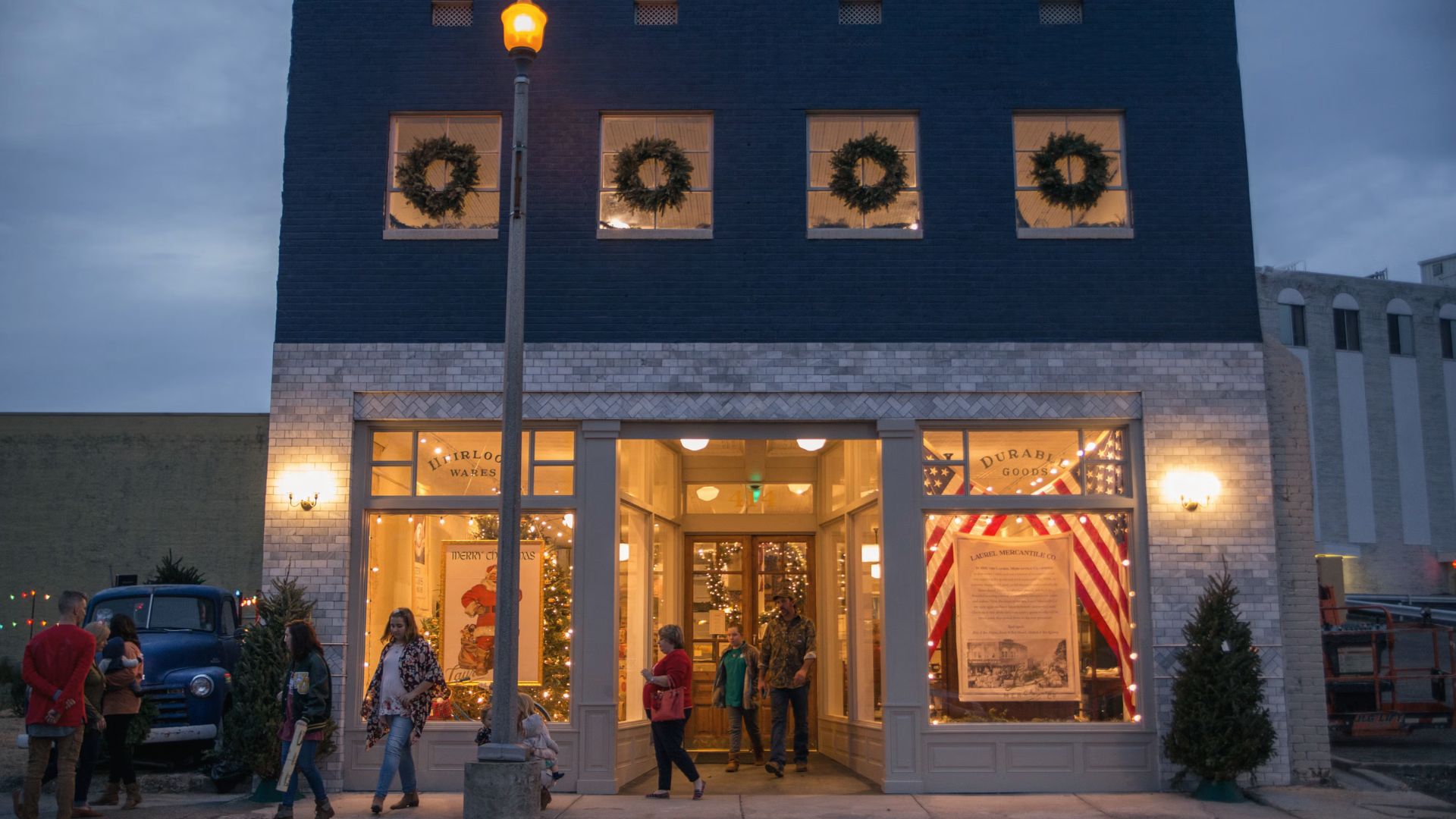 Laurel Mercantile Co. storefront in downtown Laurel at dusk, decorated with Christmas wreaths and string lights.