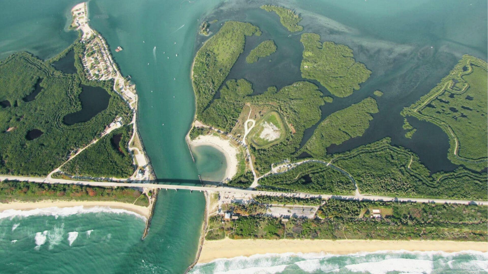 Aerial view of coastal inlet, beach, bridge, green mangroves, roads, and turquoise ocean water